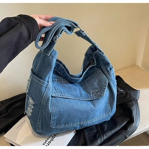 Dettaglio borsa a tracolla in denim blu con bordi sfrangiati e fibbia in metallo regolabile