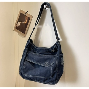 Dettaglio di una borsa a tracolla in denim blu scuro con cuciture bianche decorative