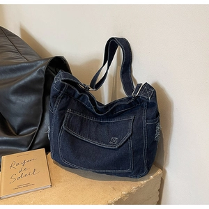 Dettaglio della borsa a tracolla in denim blu scuro con cuciture bianche e tasca