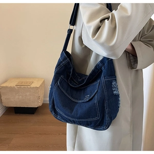 Dettaglio della borsa in denim blu scuro con cuciture bianche a contrasto e bordi sfrangiati