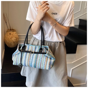 Detail of hand-woven straw tote bag with blue wavy stripes and black leather buckles