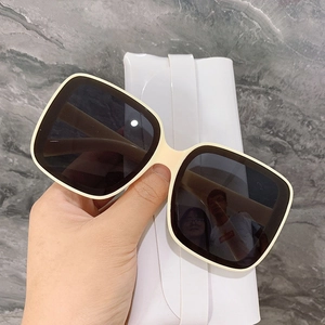 Oversized square cream sunglasses with dark grey lenses held over marble background