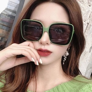 Oversized square green sunglasses with dark lenses worn by a model in outdoor lighting