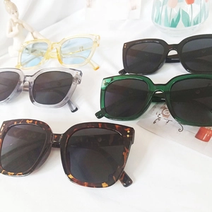 Flat lay of square-frame sunglasses in various colors on white fabric with artistic props