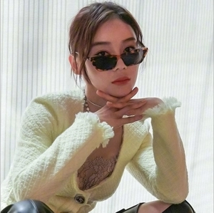 Close-up of knit cardigan with fringe trim, buttons, and tortoiseshell sunglasses