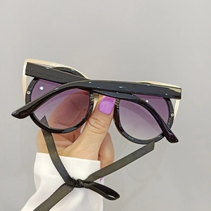 Close-up of black cat-eye sunglasses with gold metal trim and purple gradient lenses