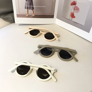 Retro round thick frame sunglasses in cream, khaki, and white on a minimalist magazine