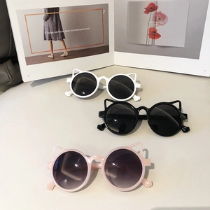 Kids' cat-ear sunglasses in black, white, and pink with UV protection on a magazine