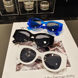 Three pairs of vintage wide-frame cat-eye sunglasses in blue, black, and white on a magazine