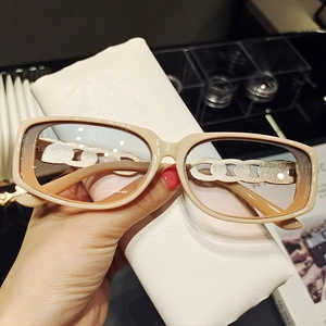 Détail de lunettes de soleil beiges avec branches en chaîne dorée et étui en cuir