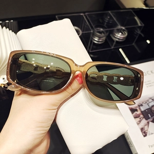 Détail de lunettes de soleil marron tendance avec branches chaîne dorée et verres verts