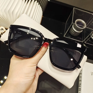 Detail of hand-held black square sunglasses with dark lenses and a white textured pouch