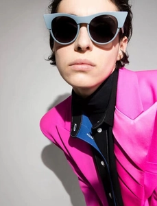 Fashionable blue cat-eye sunglasses with dark lenses worn by a model in a pink blazer