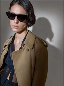 Chic female model wearing cat-eye sunglasses and a classic khaki double-breasted trench coat
