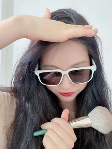 Close-up of white oversized square sunglasses with dark lenses and a makeup brush tool