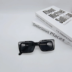 Close-up of black rectangular sunglasses with premium thick frames on white books