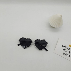 Détail de lunettes de soleil en forme de cœur avec pois blancs et verres foncés sur fond gris