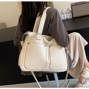 Detail of a beige textured faux leather tote with large pockets and metal rivet accents