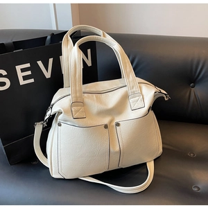Detail of creamy white tote bag with lychee texture and dual front pockets on black sofa