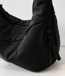 Detail of black nylon dumpling bag featuring a woven rope zipper pull and textured fabric