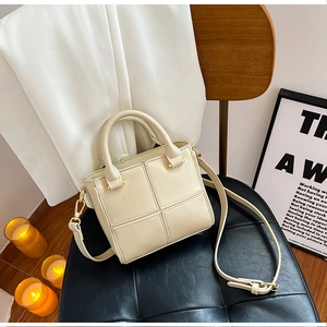Détail du sac seau crème avec surpiqûres carrées sur un siège en cuir noir avec bougies