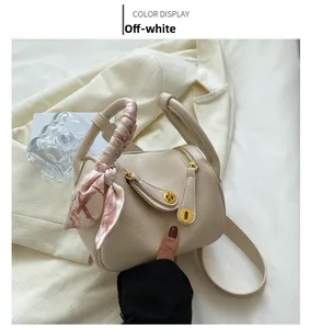 Détail d'un sac à main beige en cuir litchi avec ferrures dorées et un foulard en soie