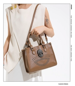 Close-up of brown leather tote bag with skull stud detailing and adjustable strap