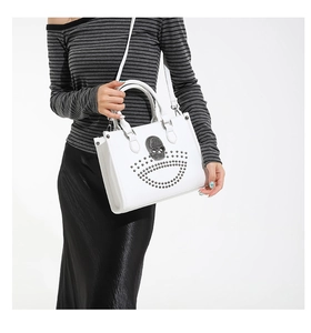 Close-up of a white leather tote with a metal skull and rivets on a fashion model