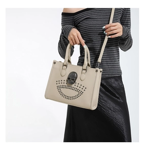 Close-up of beige tote bag featuring metallic skull and rivet details on the front panel