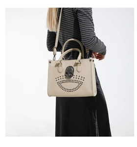 Detailed view of cream tote bag featuring vintage skull ornament and metal studs on a model