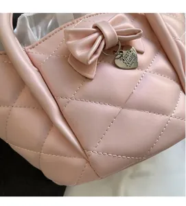 Close-up of pink quilted handbag with leather bow and heart-shaped metal pendant charm