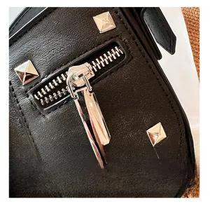 Close-up of silver metal zipper and pyramid studs on a black textured leather bag