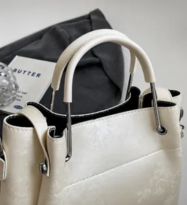 Primer plano de bolso tote crema con asa metálica y grabado de patrón vegetal