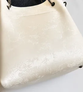 Primer plano del bolso beige con textura jacquard floral y soportes metálicos en base