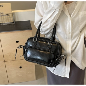 Detail of glossy black Boston bag featuring side drawstring bows and silver hardware
