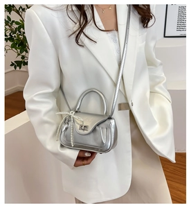 Detail of silver mini crossbody bag featuring a pearl bow charm and metal twist lock