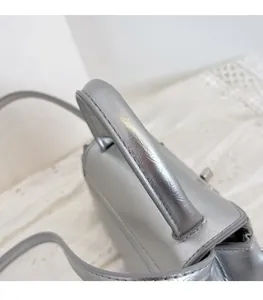 Detailed close-up of silver leather handbag handle and elegant metal twist lock closure