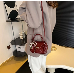 Detail of dark red PU leather crossbody bag with pearl bow charm and twist lock