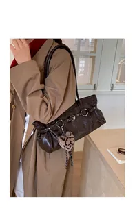 Detail of dark brown tote bag with glossy texture, buckle strap and heart leopard charm