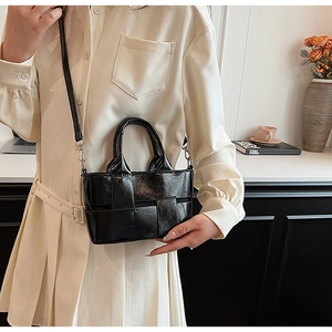 Detail of black woven texture handbag with silver hardware held by a model in a minimal setting