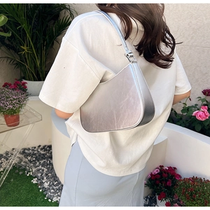 Chic silver crescent underarm bag in metallic leather worn by model in a lush garden