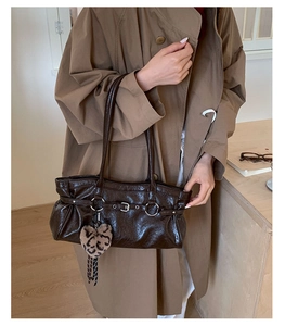 Detail of deep brown patent leather tote bag with vintage texture and heart charm