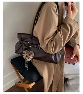 Detail of dark brown pleated tote bag with leopard heart charm and side buckle strap