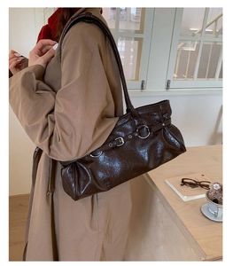 Close-up of a dark brown glossy shoulder bag with a silver buckle and pleated details