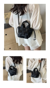Détail d'un sac seau en cuir tressé noir avec poignées et bandoulière réglable