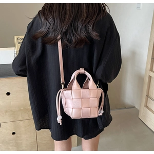 Détail d'un sac seau tressé rose avec poignée et bandoulière porté par un modèle
