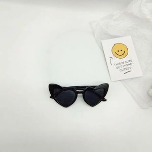 Close-up of heart-shaped black sunglasses on white background with a decorative card
