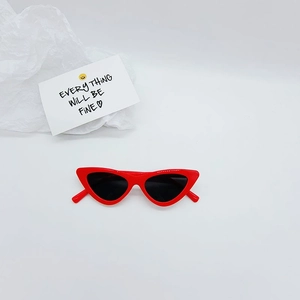 Detail of red cat-eye sunglasses for kids with dark lenses and minimalist paper background