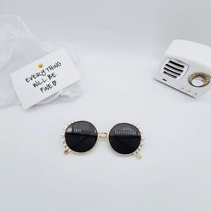 Detailed view of round metal children's sunglasses with elegant pearl trim on gold frames