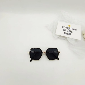 Close-up of hexagonal kids sunglasses with black frames and gold metal hinge details